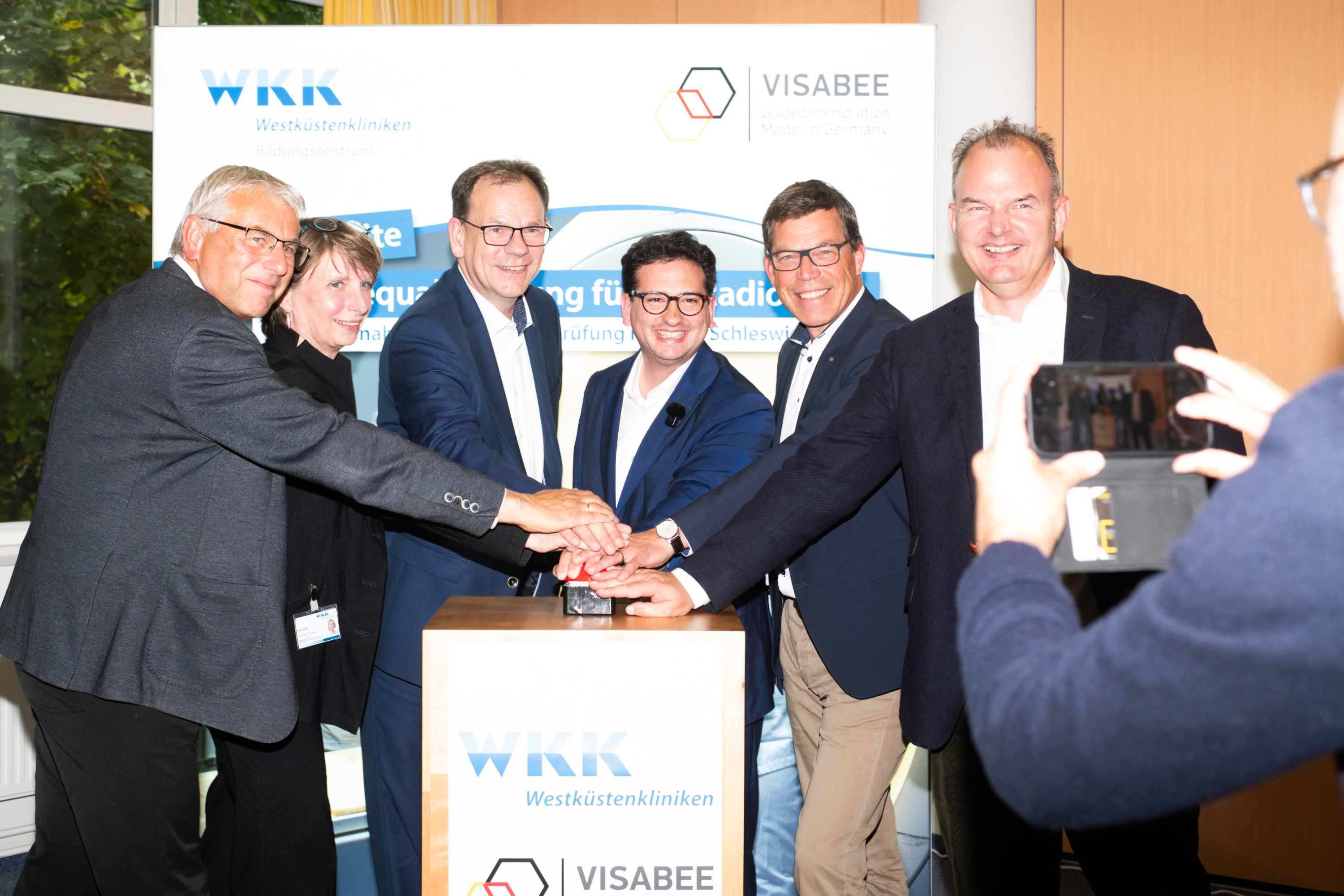 Bastian Mahmoodi steht mit fünf weiteren Personen beim offiziellen Start eines Projekts von VISABEE und den Westküstenkliniken.